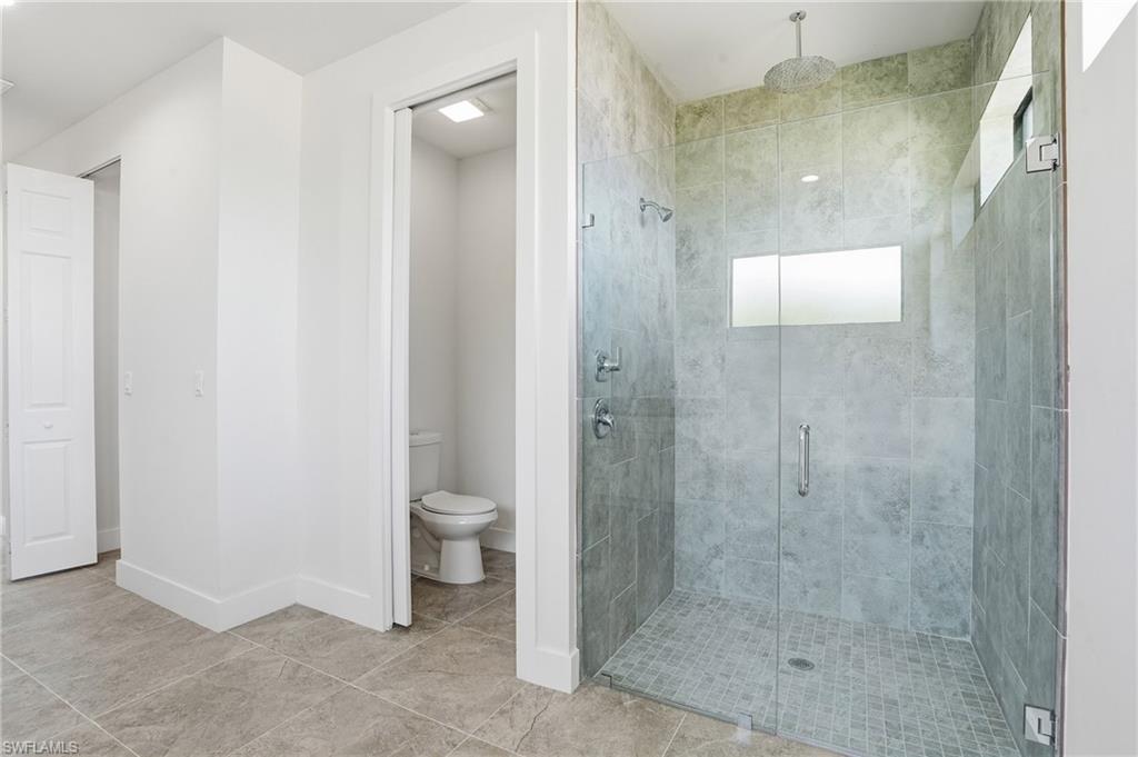 Glass-enclosed shower featuring a rainfall showerhead, wall-mounted fixtures, and a transom window, all surrounded by large format tile