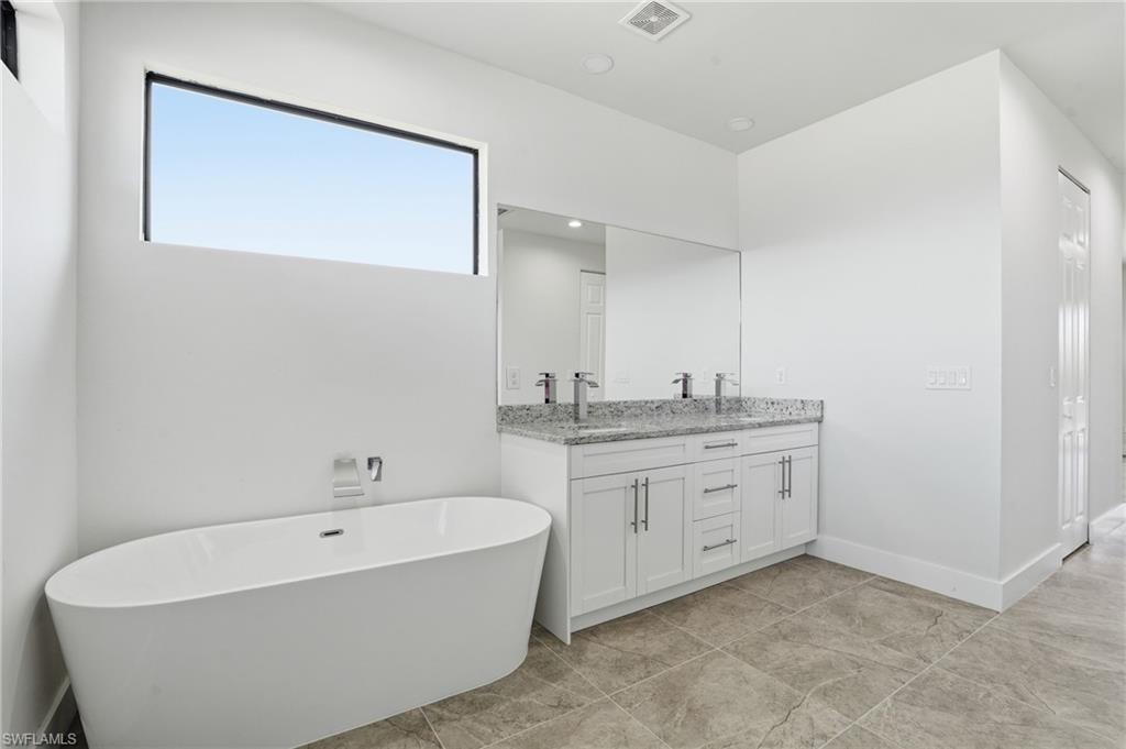 Modern bathroom featuring a freestanding soaking tub, a horizontal window, a double vanity with a stone countertop, and large format floor tiles