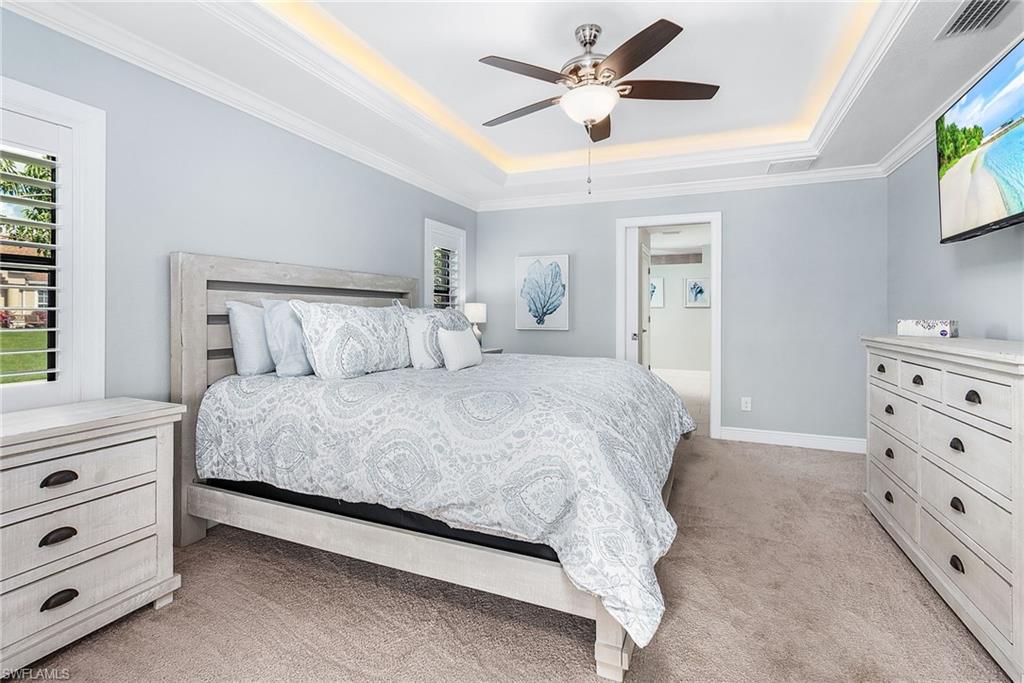 Bedroom with crown molding, a tray ceiling, visible vents, and light colored carpet