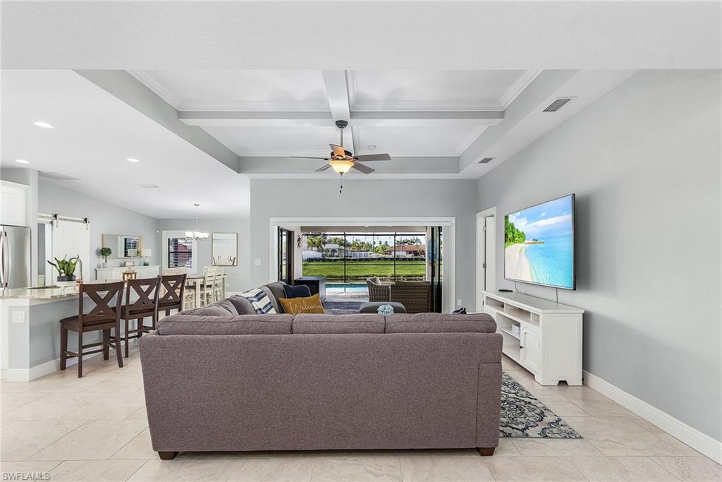 Living room with ceiling fan with notable chandelier, coffered ceiling, visible vents, baseboards, and beam ceiling