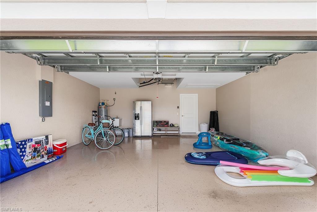 Garage featuring electric panel, stainless steel refrigerator with ice dispenser, and electric water heater