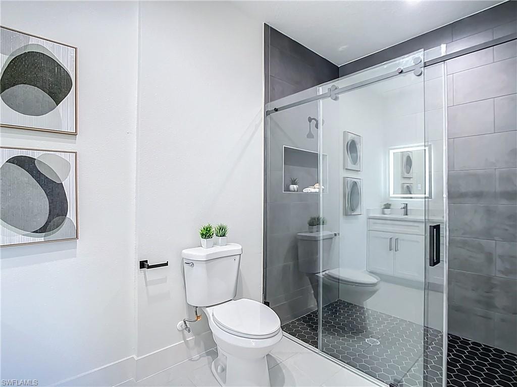 Contemporary bathroom featuring a frameless glass shower enclosure with a sliding door, dark hexagon tile shower flooring, and light gray subway tile walls