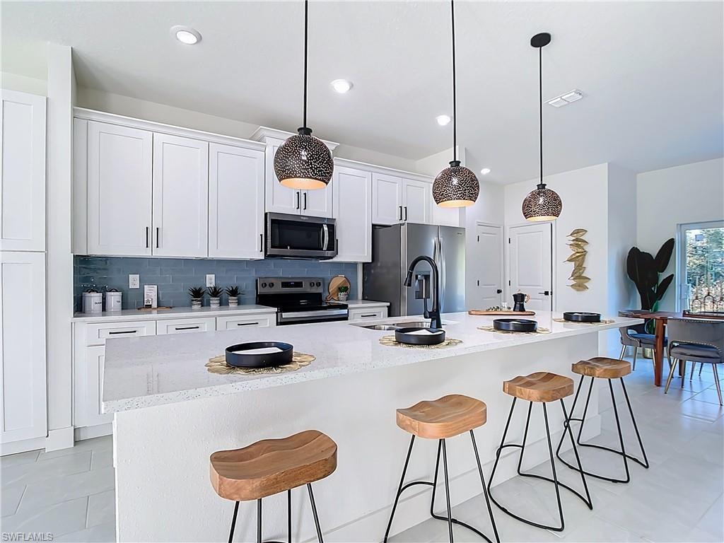 Modern kitchen featuring a large central island with seating, white shaker cabinetry, stainless steel appliances, and a blue subway tile backsplash