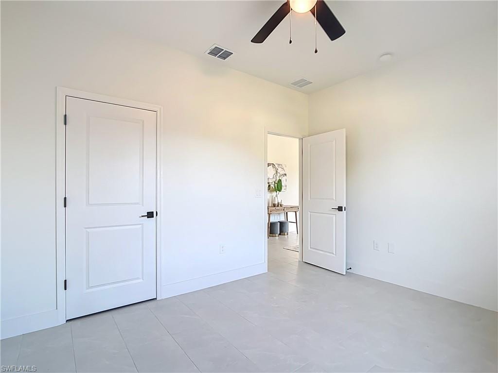 Spacious room featuring light-colored tile flooring, white walls, and a ceiling fan with black blades