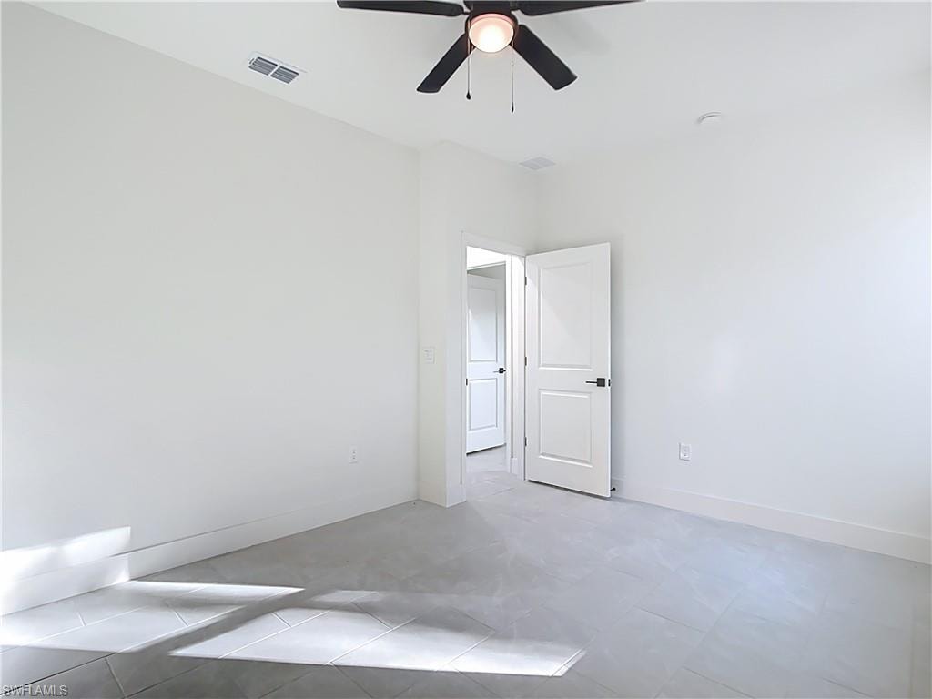Spacious interior room featuring light gray tile flooring, crisp white walls, a modern ceiling fan with integrated lighting, and white interior doors with black hardware