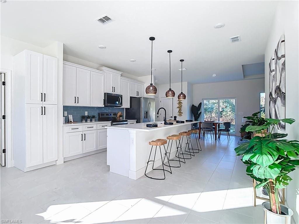 Contemporary kitchen featuring white shaker cabinetry, an expansive central island with seating, a blue subway tile backsplash, and a full suite of black appliances