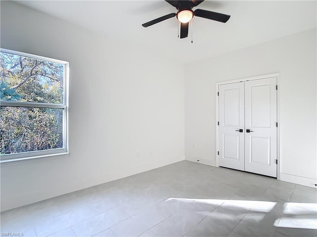 Spacious room featuring light gray tile flooring, a contemporary ceiling fan with integrated lighting, and a double-door closet with matte black hardware