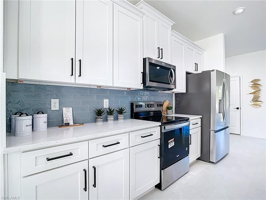 Modern kitchen featuring white shaker cabinetry with dark hardware, a light-colored countertop, and a blue subway tile backsplash