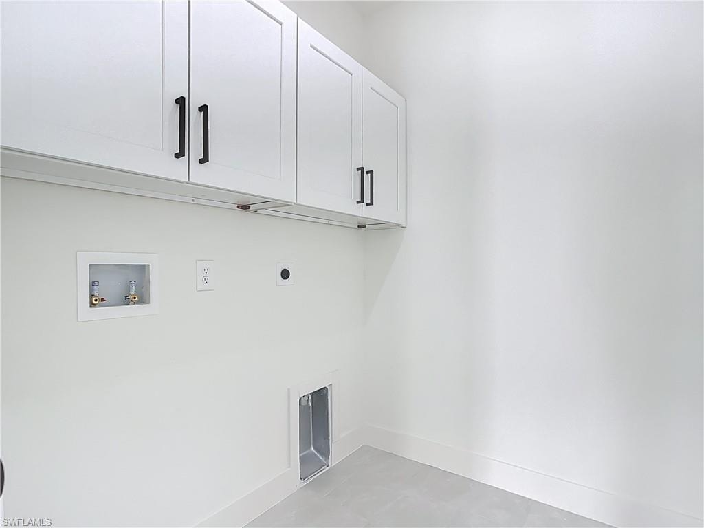 Utility room featuring overhead white cabinetry with black hardware, washer/dryer hookups, and light-toned flooring