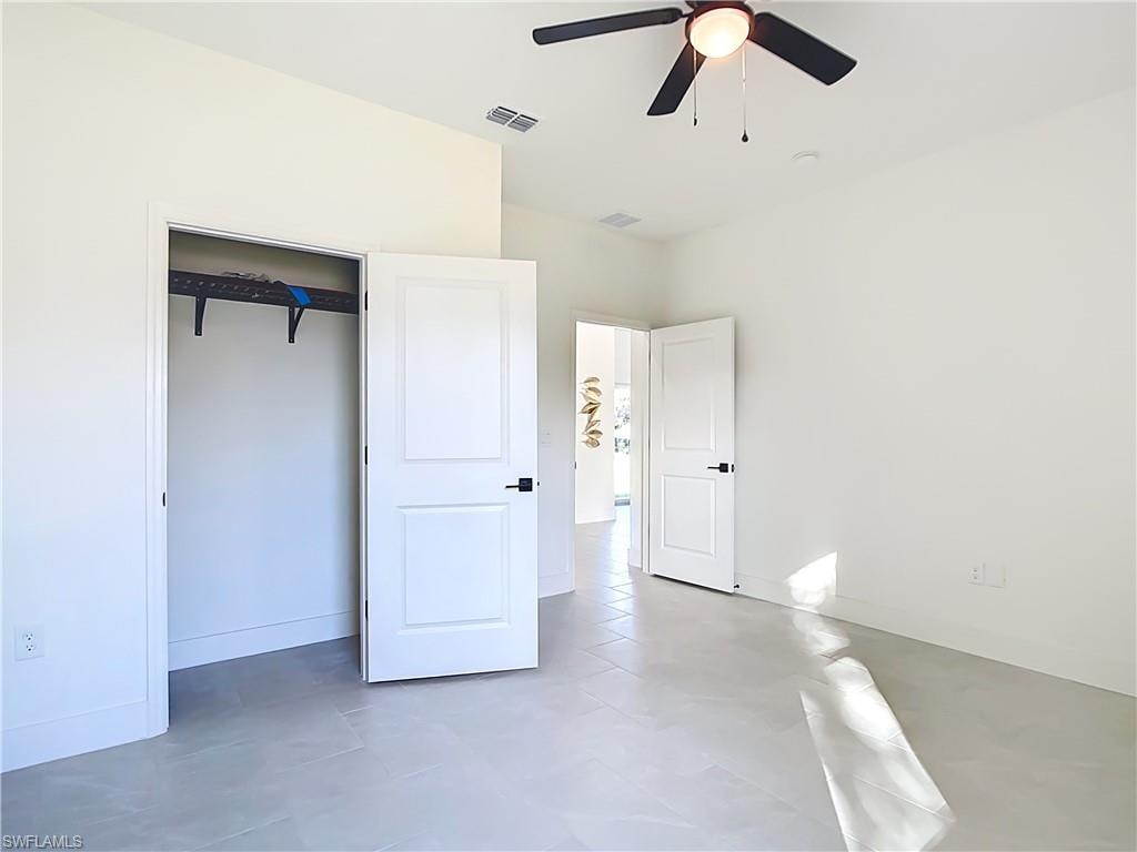 Spacious room featuring light-toned tile flooring, a dark-toned ceiling fan, and white doors with matte black hardware