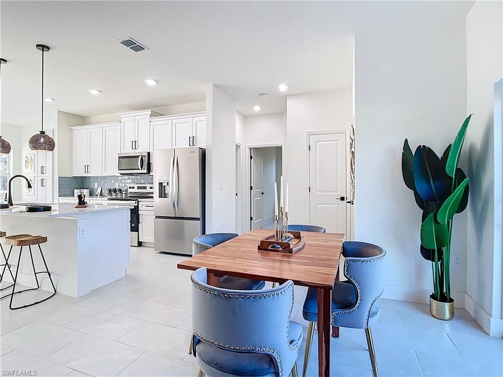 Open-concept kitchen and dining area featuring white cabinetry, stainless steel appliances, and a subway tile backsplash