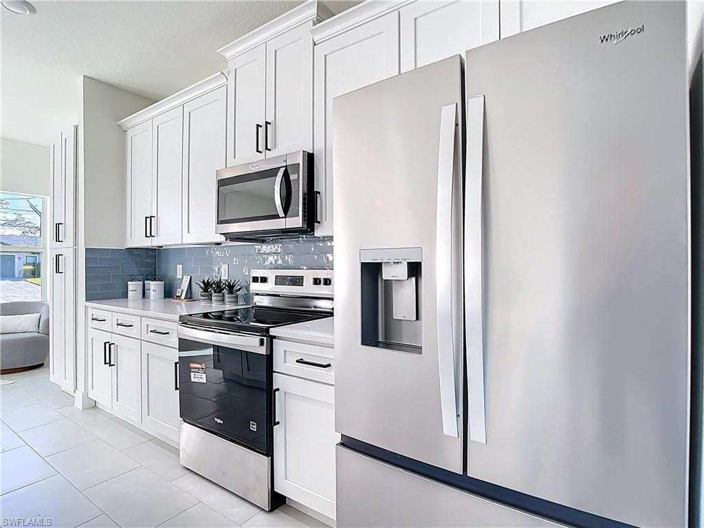 Modern kitchen featuring stainless steel appliances, white shaker cabinetry, light-toned countertops, a blue subway tile backsplash, and tile flooring
