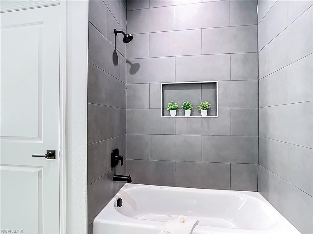 Bathtub shower featuring large format gray tile surround, matte black fixtures, and a recessed shower niche