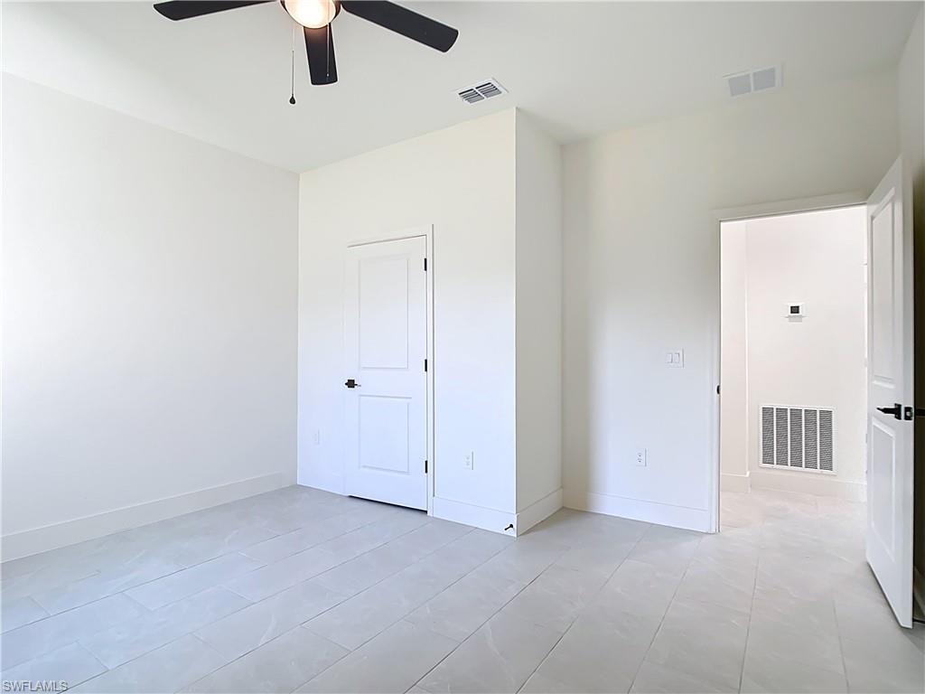 Spacious room featuring light-toned tile flooring, clean white walls, and a ceiling fan with integrated lighting
