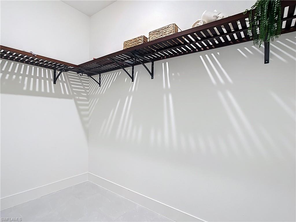 White-painted walls featuring L-shaped wood-slat shelving with black metal brackets and light gray tile flooring