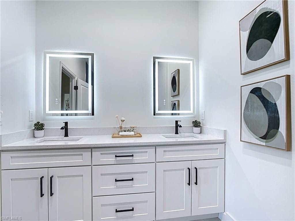 Dual vanity featuring white shaker cabinetry, matte black hardware, integrated sinks, and light-toned countertops