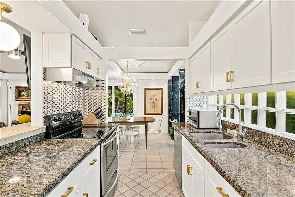 Kitchen featuring appliances with stainless steel finishes, under cabinet range hood, a sink, light tile patterned floors, and backsplash