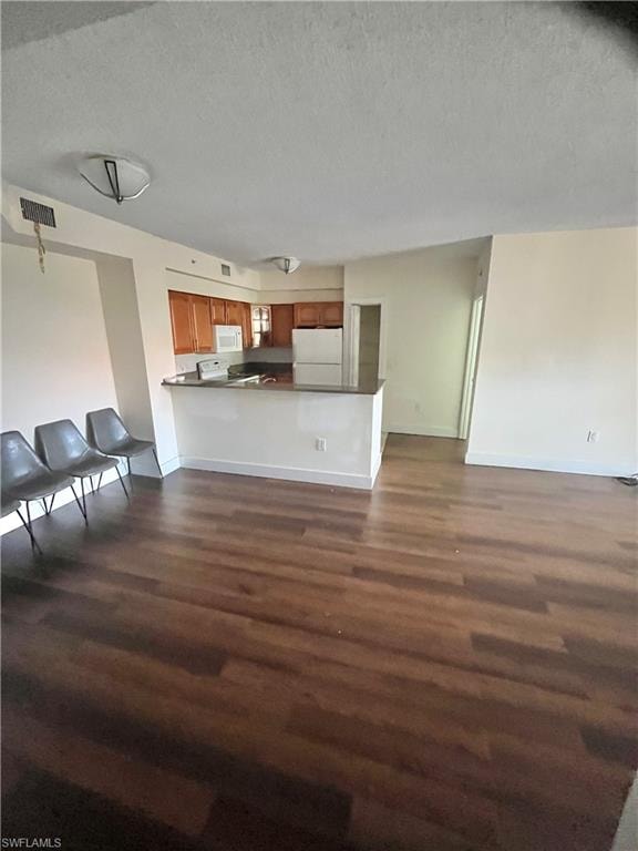 Open-concept living space featuring wood-finish flooring, a kitchen island with a dark countertop, wood cabinetry, and recessed lighting
