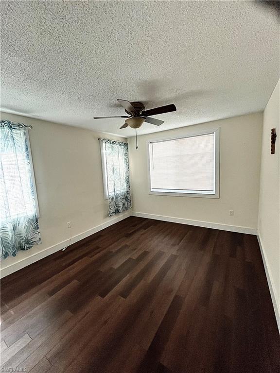 Interior room featuring dark wood-finish flooring, white walls, and a ceiling fan with integrated lighting