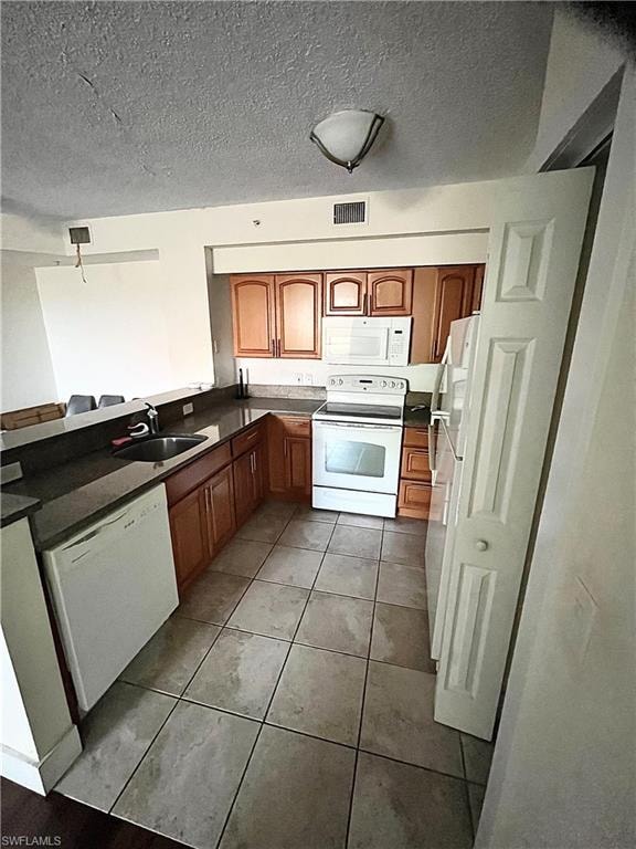 Kitchen featuring wood cabinetry, dark countertops, a built-in sink, and white appliances including a range, microwave, and dishwasher
