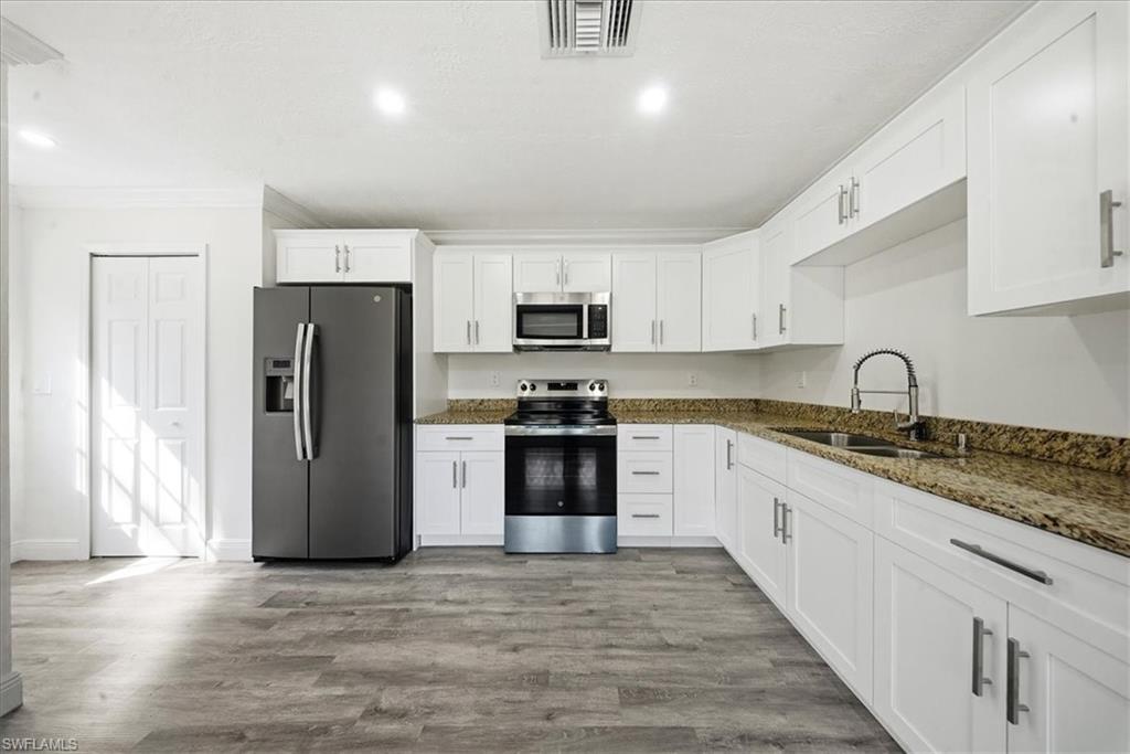 Kitchen featuring stainless steel appliances, white cabinetry, dark stone countertops, light wood finished floors, and ornamental molding