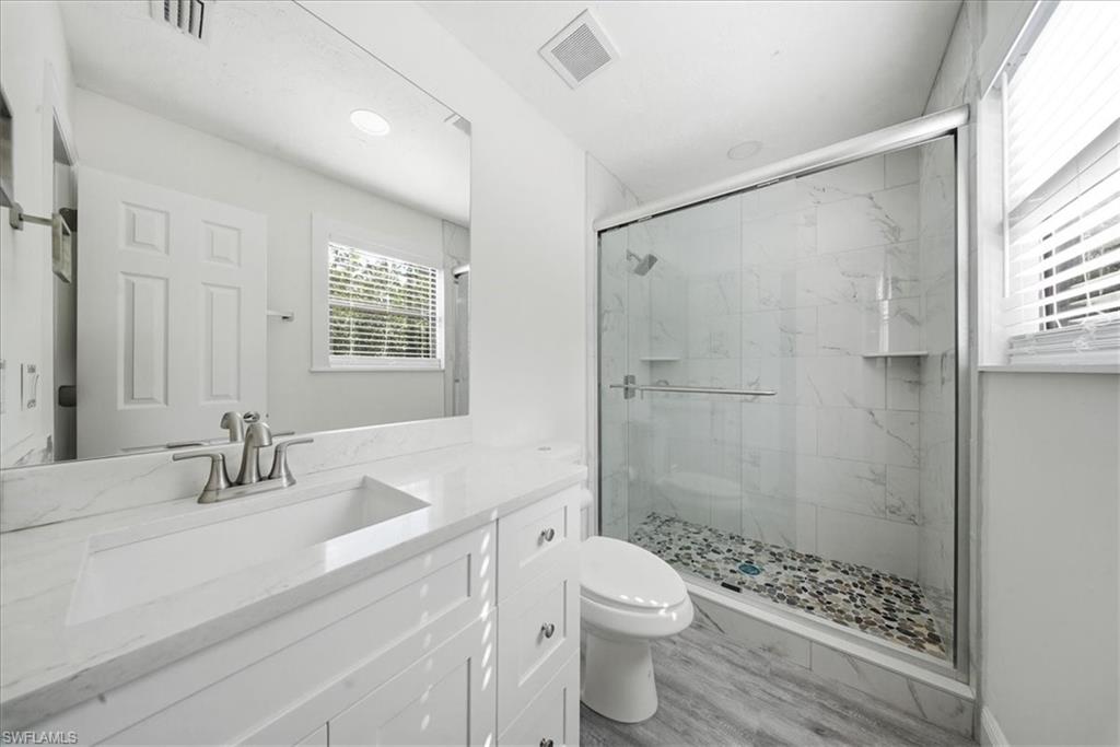 Bathroom featuring vanity, a marble finish shower, and light wood-style floors
