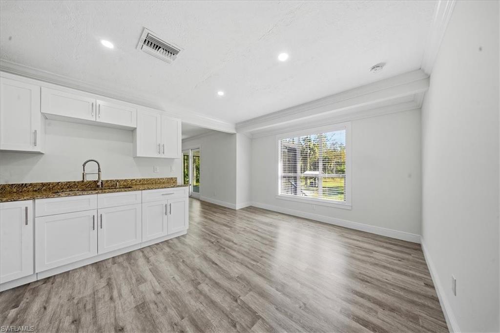 Kitchen with white cabinetry, ornamental molding, light wood finished floors, recessed lighting, and dark stone counters