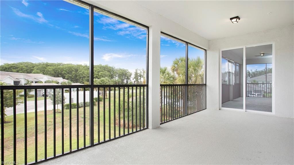 Screened balcony featuring expansive outdoor space, concrete flooring, black metal railings, and a white ceiling with a flush-mount light fixture