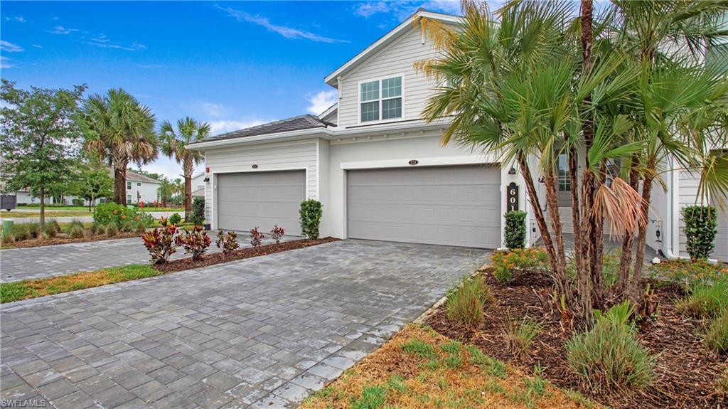 Contemporary exterior featuring light gray siding, dual garages with gray doors, and a paver driveway