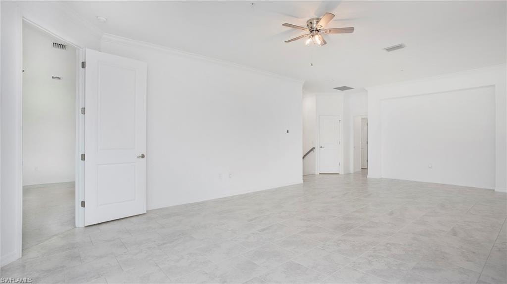 Spacious interior with neutral wall tones, large format tile flooring, crown molding, and a ceiling fan with integrated lighting
