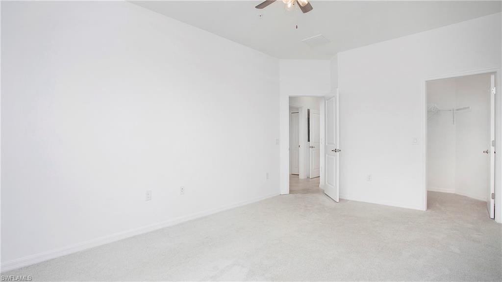 Spacious room featuring light-colored carpeting, white baseboards, and a ceiling fan