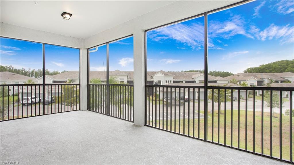 Expansive screened balcony featuring light gray carpet, a black metal railing, a ceiling-mounted light fixture, and a white painted ceiling