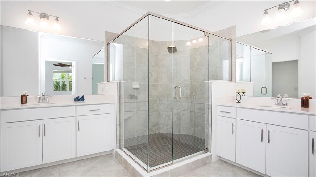 Spacious bathroom featuring a frameless glass shower enclosure with tiled walls, dual vanity sinks with white cabinetry, polished chrome fixtures, and large wall-mounted mirrors