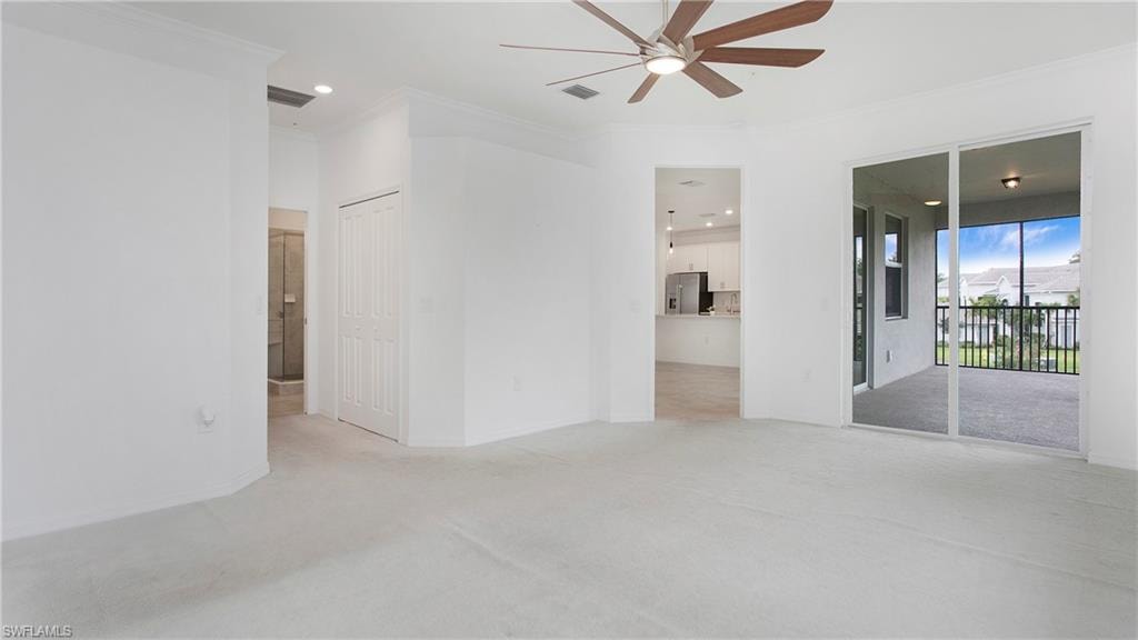 Spacious carpeted room featuring crown molding, a ceiling fan, and sliding glass doors opening to a screened balcony
