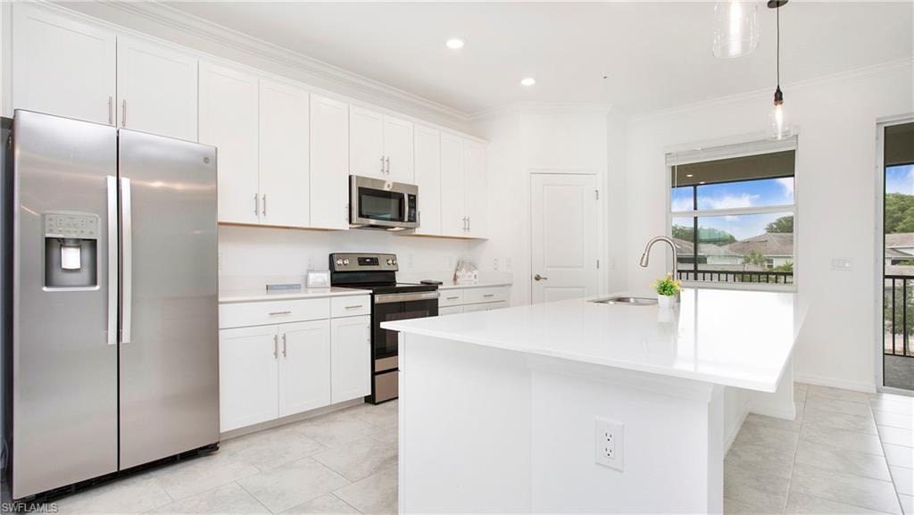 Modern kitchen featuring white cabinetry, stainless steel appliances, a center island with a sink, light-toned flooring, and a large window