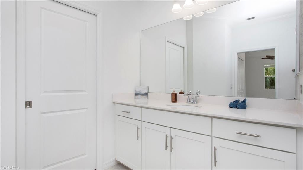 Full vanity with a white countertop and integrated sink, white cabinetry with silver hardware, large wall-mounted mirror, and overhead vanity lighting