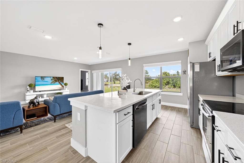 Kitchen featuring white cabinetry, appliances with stainless steel finishes, open floor plan, pendant lighting, and a kitchen island with sink