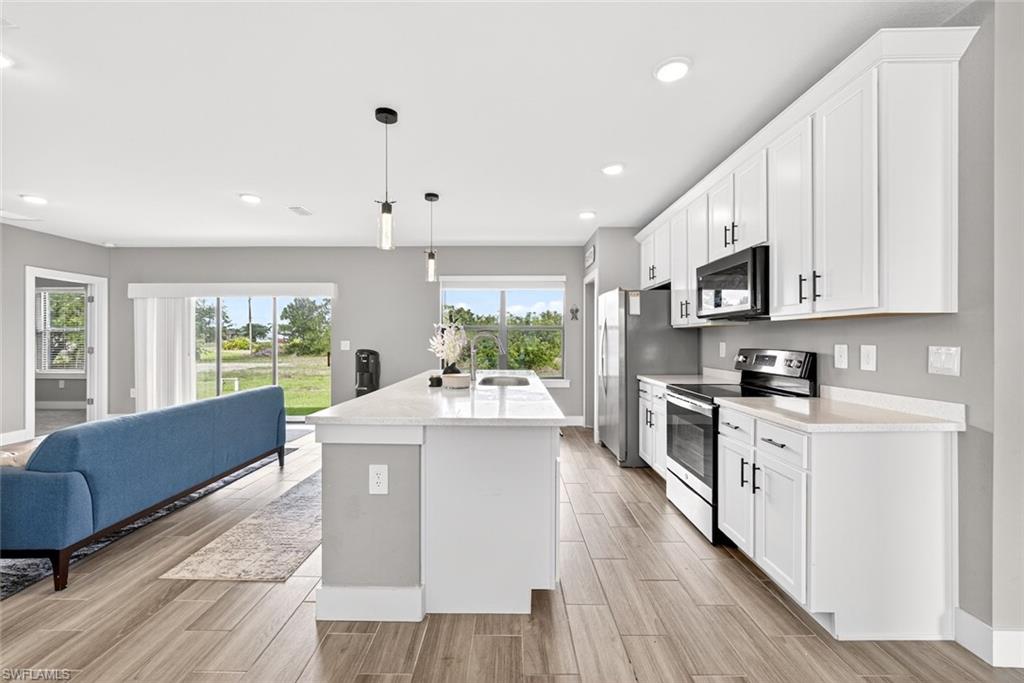 Kitchen featuring white cabinetry, stainless steel appliances, open floor plan, decorative light fixtures, and a center island with sink