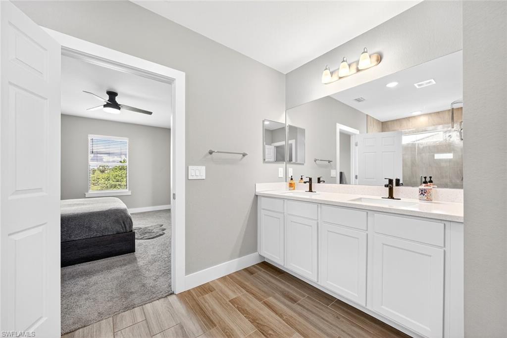 Ensuite bathroom featuring double vanity, a stall shower, wood finish floors, and ceiling fan