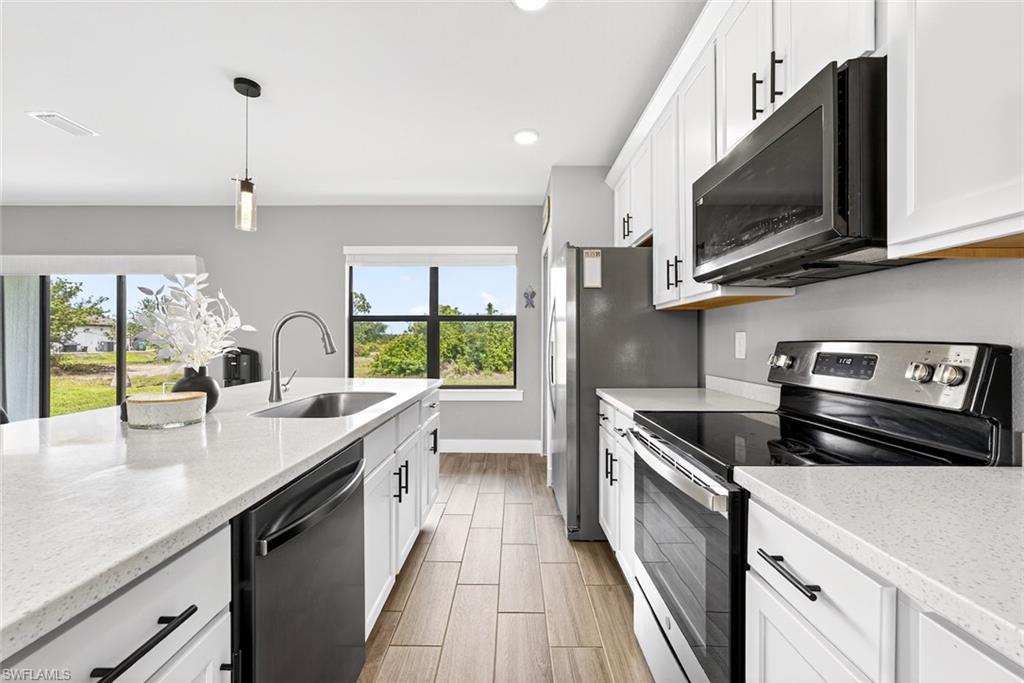 Kitchen with stainless steel appliances, white cabinetry, light stone counters, pendant lighting, and recessed lighting