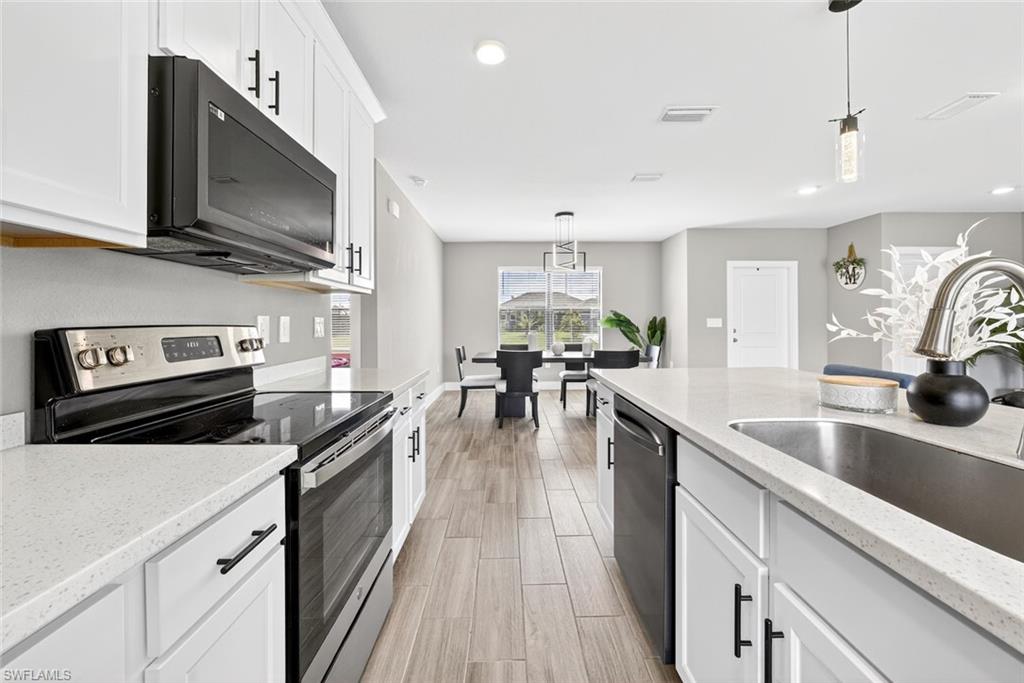 Kitchen featuring stainless steel appliances, white cabinetry, pendant lighting, light stone countertops, and recessed lighting
