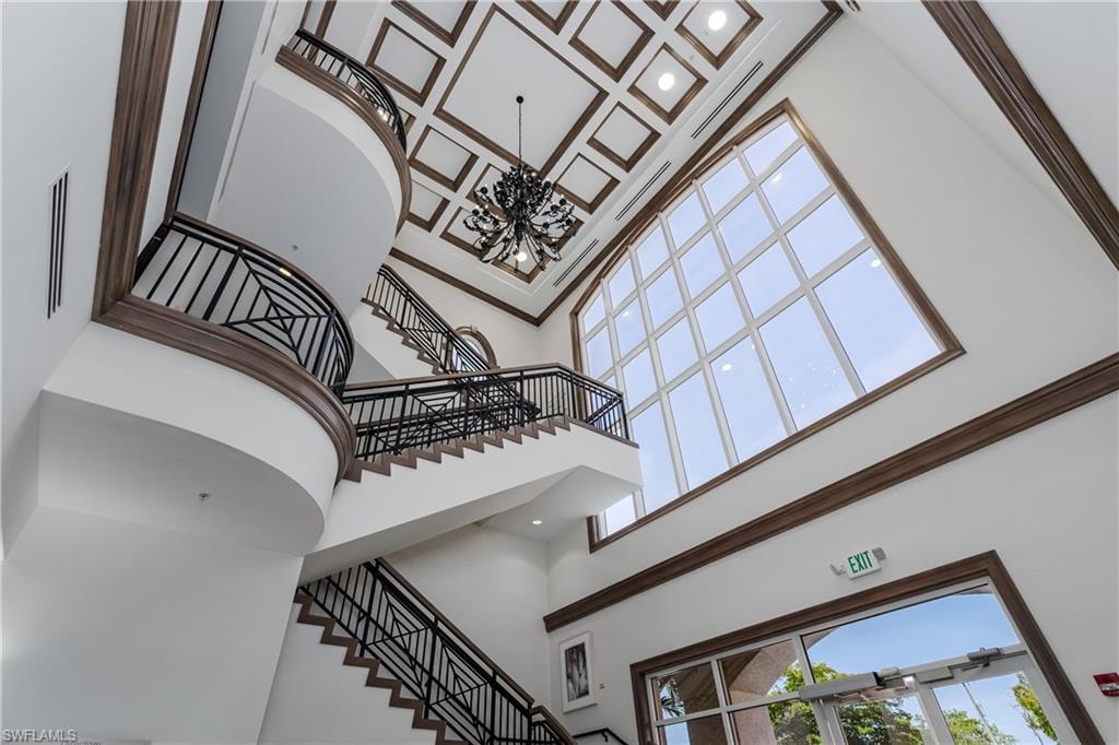 Grand foyer featuring a coffered ceiling, multi-level staircase with decorative wrought iron railings, and a prominent arched window wall