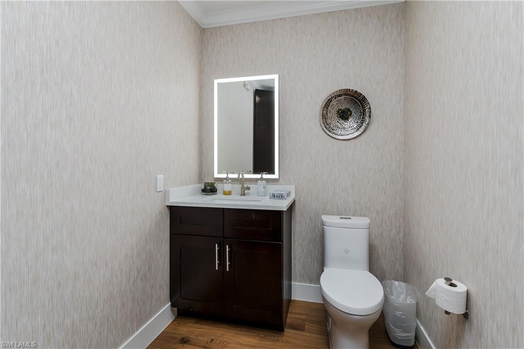 Bathroom featuring a dark wood vanity with a white countertop, an illuminated mirror, and wood-finish flooring