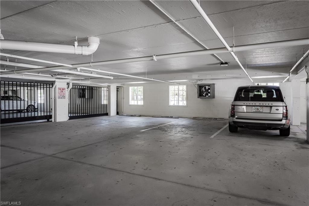Secure covered parking garage featuring concrete flooring, a white painted ceiling with exposed piping, and a gated entry system