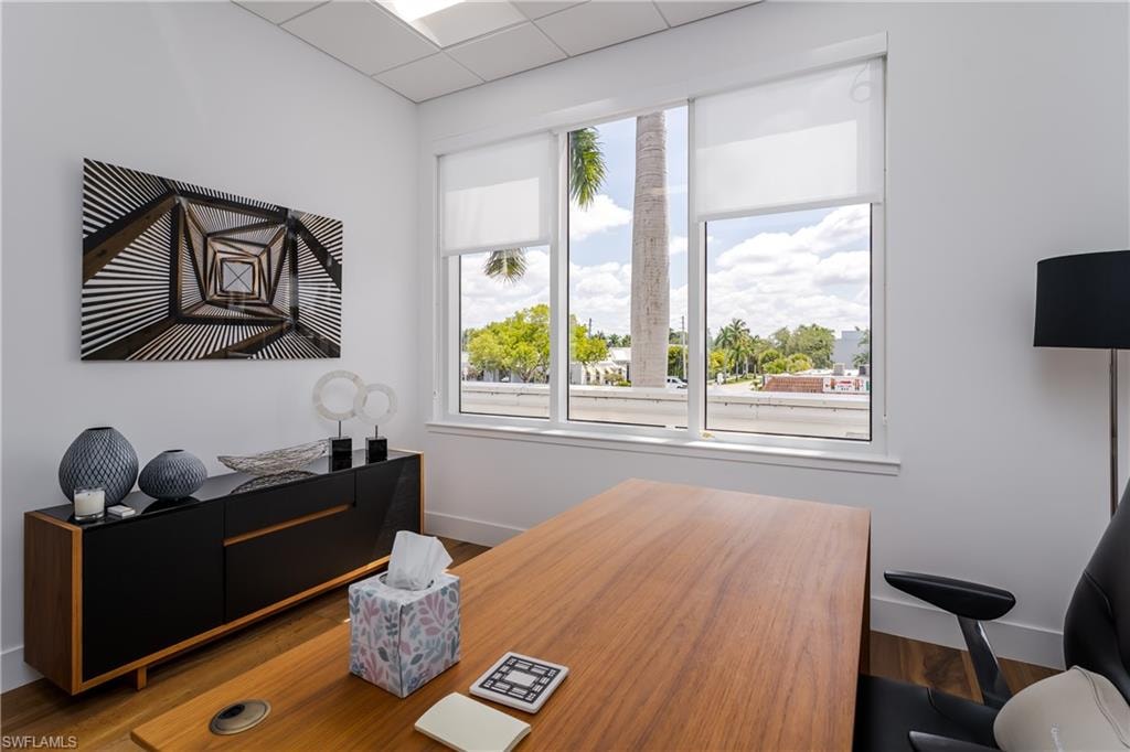 Expansive window with white roller shades, white walls, wood-finish flooring, and a drop ceiling with recessed lighting