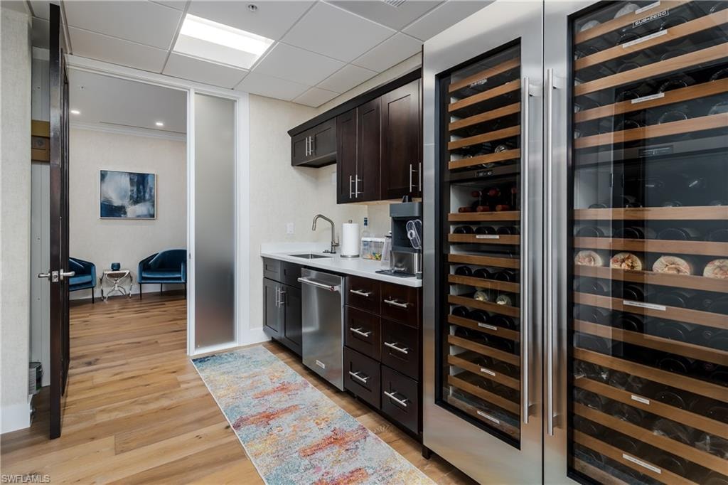 Integrated wet bar featuring dark wood-finish cabinetry, a stainless-steel under-counter dishwasher, and a white countertop