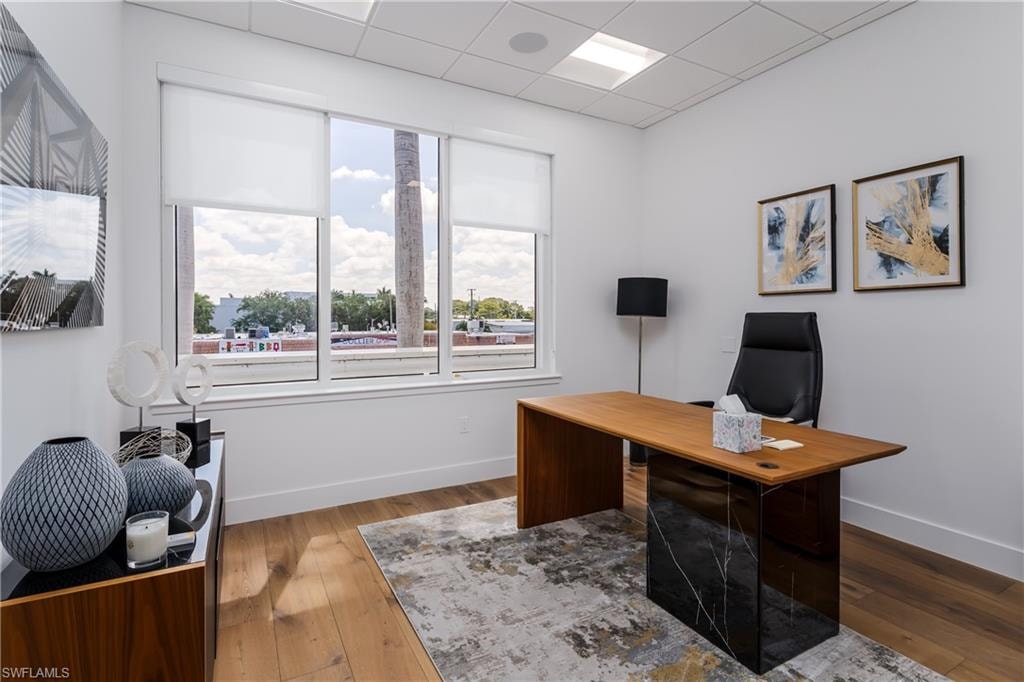 Bright interior space featuring wood-finish flooring, white walls, and a large window with roller shades