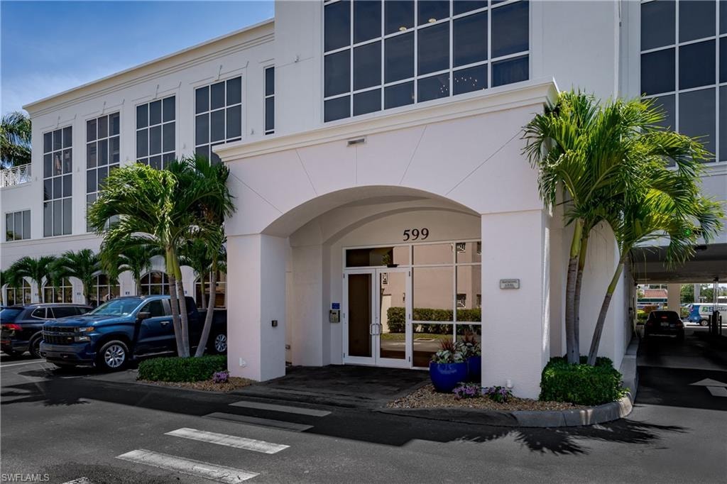 Building entrance featuring a prominent arched portico, full-light glass double doors, large multi-pane windows, palm trees, and a paved parking area