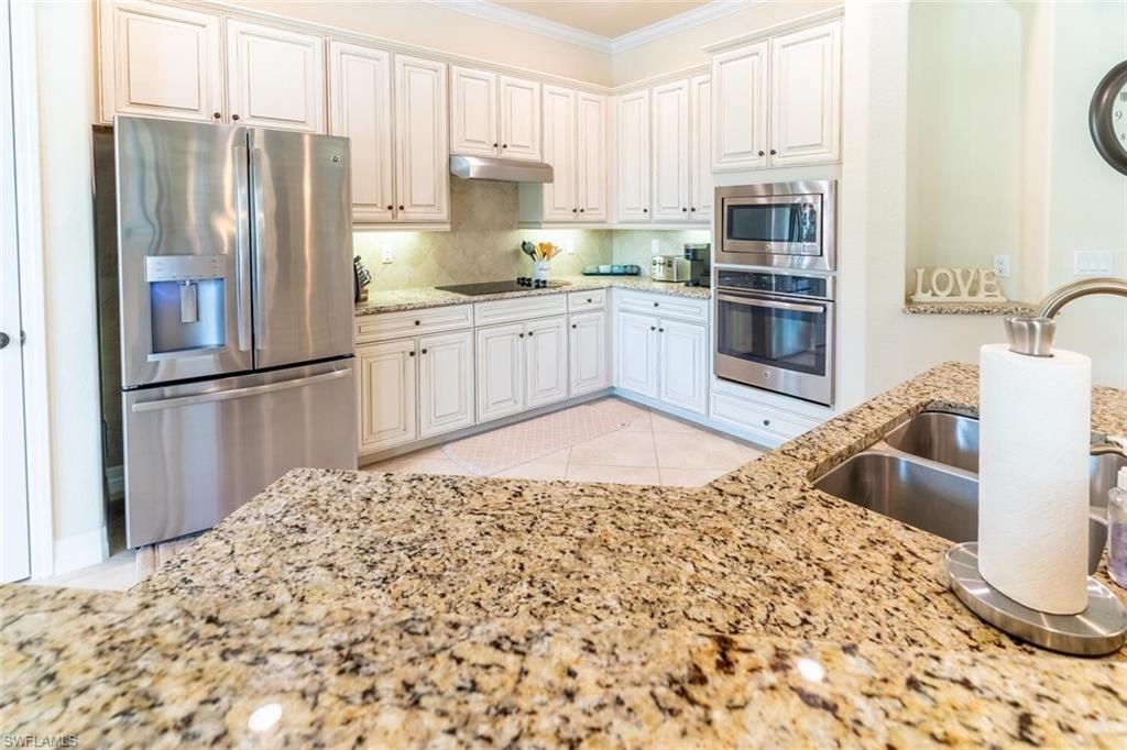 Kitchen with light tile patterned flooring, stainless steel appliances, backsplash, light stone counters, and white cabinets