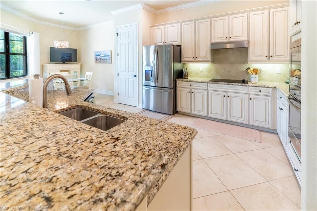 Kitchen with black appliances, light stone countertops, light tile patterned floors, tasteful backsplash, and sink